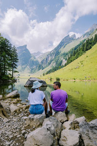 Rear view of people on rock by mountains against sky