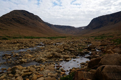 Scenic view of stream flowing through rocks against sky