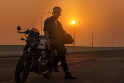 Motorcycle driver in a helmet and leather jacket stands on the road next to a sports motorcycle