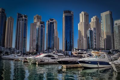 Boats sailing in river by city against clear sky