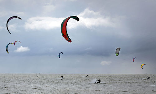 People kiteboarding in sea against cloudy sky