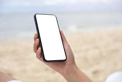 Low angle view of hand holding smart phone at beach