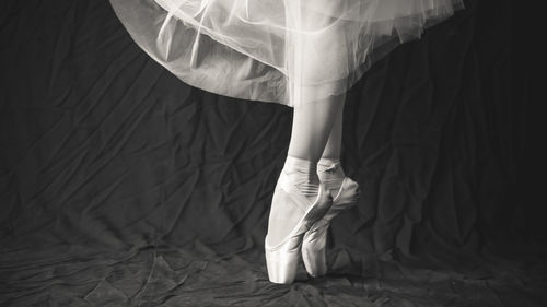 Low section of female ballet dancer dancing against black backdrop