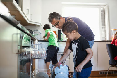 Father and son arranging plates in dishwasher at kitchen