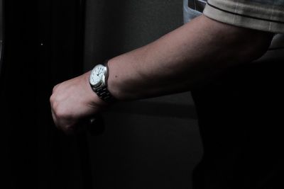 Close-up of man hand holding clock against black background