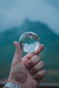 Cropped hand holding crystal ball against sky