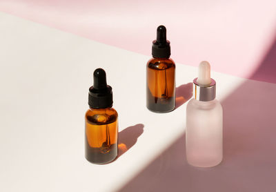 Three transparent amber and frozen glass dropper bottles with liquid inside on pink background 