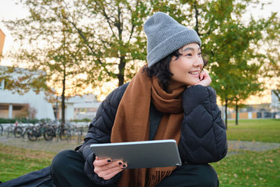 Young woman using digital tablet while sitting on field