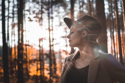 Young woman with eyes closed by tree trunk in forest