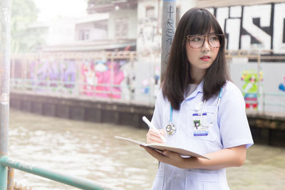 Female doctor holding book while looking away standing outdoors