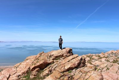 Full length of mid adult man standing on rock by sea against sky