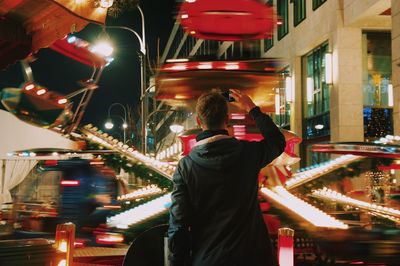 Rear view of woman photographing illuminated city at night