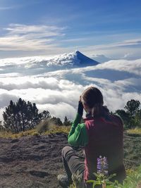 Rear view of woman sitting on mountain against sky