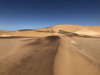 Sand dunes in desert against clear blue sky