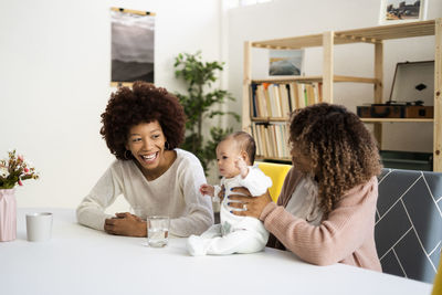 Mother with cute daughter by happy aunt at table in living room