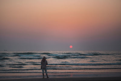 Silhouette woman standing at beach during sunset