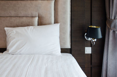 White pillow on bed by electric lamp at hotel