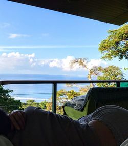 Low section of man sitting by sea against sky
