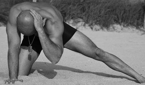 Midsection of shirtless man lying on sand at beach