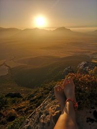 Low section of woman with arms raised standing on mountain against sky during sunset