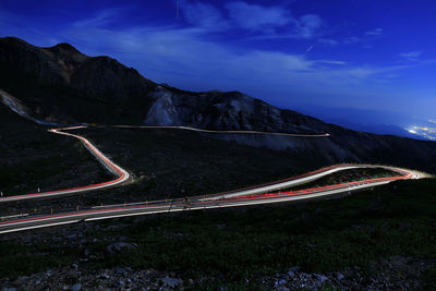 Light trails on road by mountains against sky