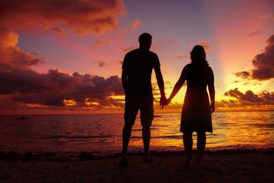 Silhouette friends standing at beach against sky during sunset