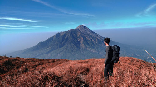 Rear view of man standing on mountain against sky