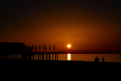 Silhouette people on beach against sky during sunset