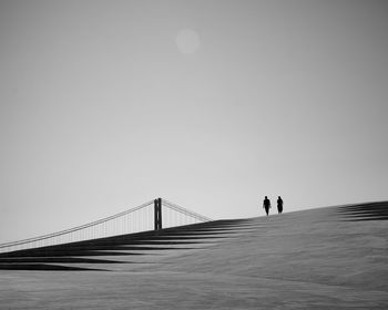 People on suspension bridge against clear sky