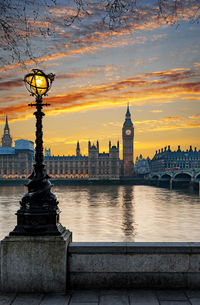 Westminster bridge by big ben over thames river against sky during sunset in city