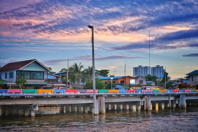 Sailboats moored on river by buildings against sky during sunset