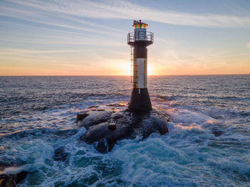 Lighthouse by sea against sky during sunset