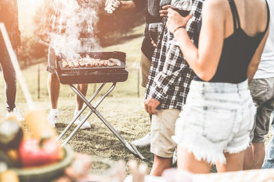 Midsection of people standing by barbecue grill on field