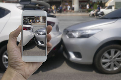 Close-up of cropped hand photographing cars on street with smart phone