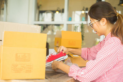 Young woman removing shoes from package on table at home