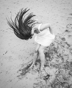 High angle view of woman tossing hair while standing on sand at beach