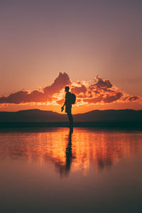 Silhouette man standing on shore against sky during sunset