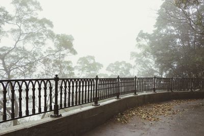 Railing by trees against sky