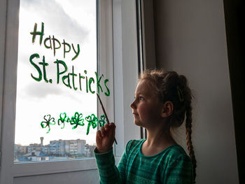 Drawing st. patrick's day child paints green three-leaved shamrock draws clover on window. stay home