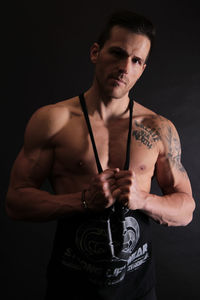 Portrait of shirtless young man against black background