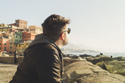 Side view of young man standing by sea against sky