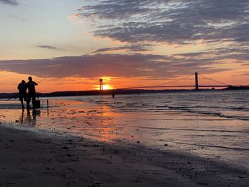 Silhouette people standing on beach against sky during sunset