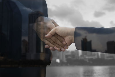 Double exposure of businessmen handshaking against cloudy sky in city