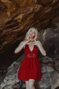 Portrait of woman making heart shape while standing against rock formation
