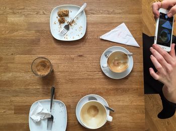 Midsection of woman photographing empty coffee cup while sitting at table