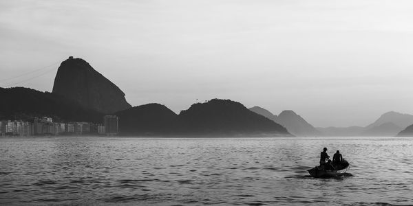 People on rock in sea against sky