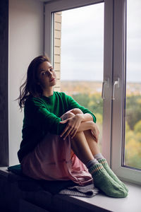 Girl sitting on the window in the green sweater in the fall