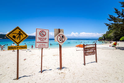 Information sign on beach against blue sky