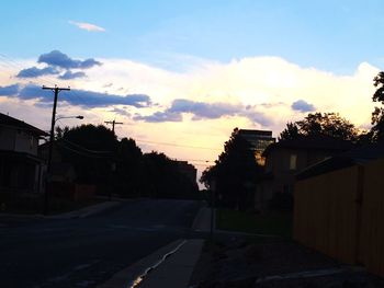 Road by silhouette buildings against sky during sunset