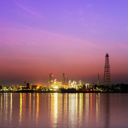 Illuminated factory by river against sky at night